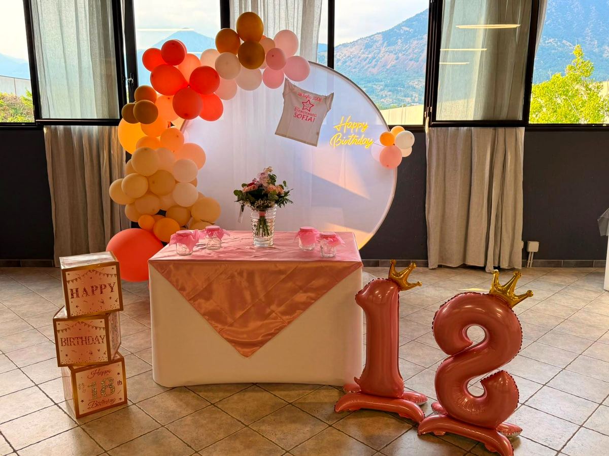Festa per i 18 anni: arco di palloncini e tavolo dolci davanti alle finestre con vista sulle montagne