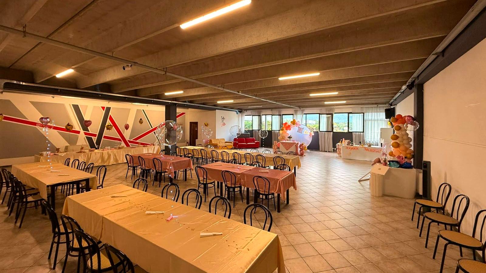 Il salone Solo Cose Belle allestito per una festa: tavolate, palloncini, angolo lounge e la parete a righe rosse e grigie