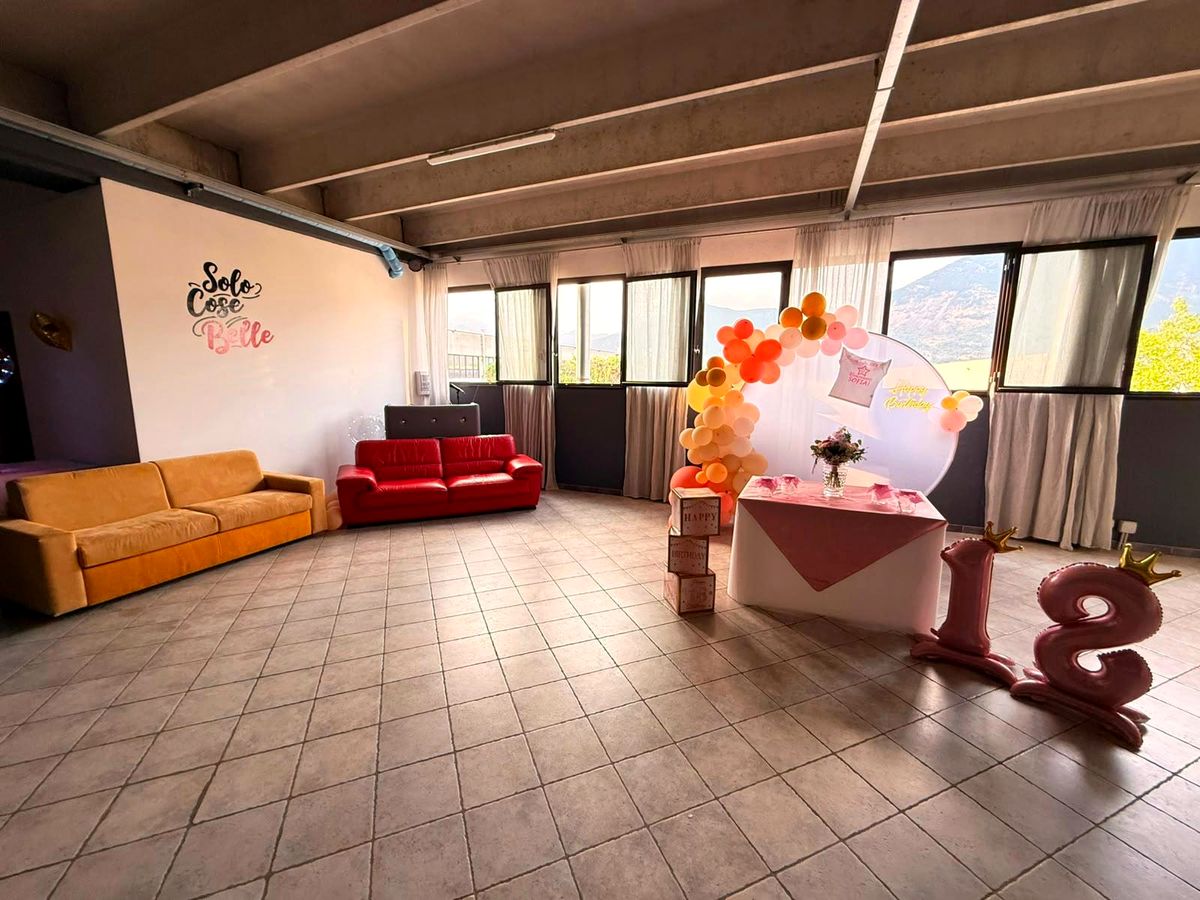 Angolo lounge con divano rosso e divano arancione, allestimento per i 18 anni e grandi finestre affacciate sulle montagne